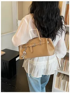 Back view of a woman carrying a textured beige leather underarm bag with a silver charm