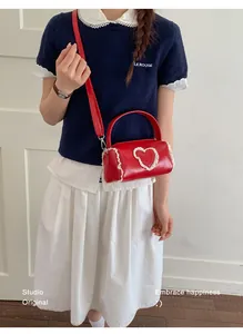 Stylish red mini cylindrical handbag with lace heart detail worn as a crossbody bag