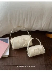 Pair of cream mini cylindrical handbags with lace heart details in a cozy scene.