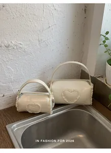 Close-up of two mini cylindrical handbags with lace heart detail in white finish.