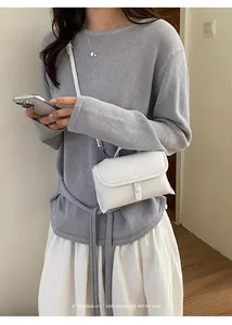 Gedetailleerd overzicht van een minimalistische witte lederen crossbodytas met casual kleding.