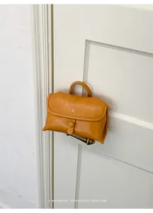 Minimalistische gele leren handtas hangend aan een klassieke witte deurklink.