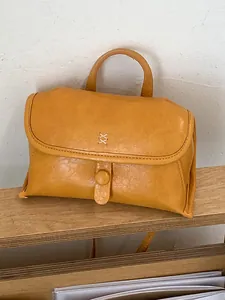 Minimalistische mosterdgele leren crossbody handtas op een houten plank geplaatst