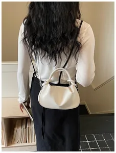 Femme en haut blanc portant un sac à main élégant en cuir de couleur crème plissé.