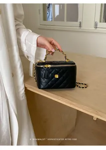 Macro detail of a black quilted mini vanity bag featuring gold chain strap and flower