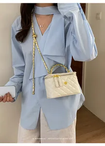 Detailed shot of a white quilted mini box bag styled with an elegant gold chain strap