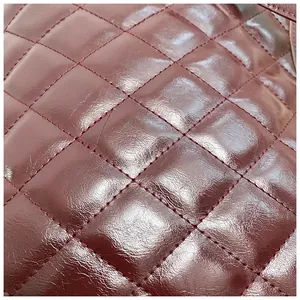 Macro detail of burgundy quilted leather with a high-gloss patent finish and fine stitching.