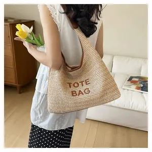 Close-up detail of hand-woven straw tote bag featuring TOTE BAG embroidery for summer