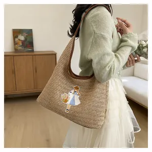 Detailed view of handmade woven straw tote bag with embroidered girl motif