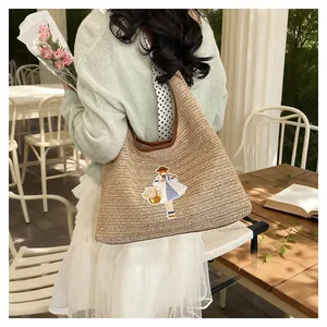 Detailed lifestyle view of large woven straw tote bag with cute girl embroidery