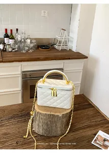 Close-up detail of white quilted vanity box bag with gold chain strap on a rustic log.