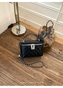 Detail of black quilted box bag with silver-tone chain strap and vanity case design