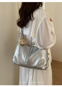 Dettaglio di una grande borsa a tracolla metallizzata argento su modella in abito bianco