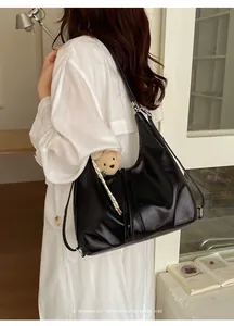 Borsa hobo in pelle nera sulla spalla di una donna con un cappotto bianco