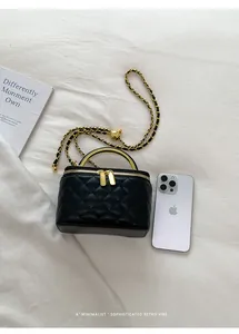 Elegant black quilted vanity box bag with gold chain strap shown next to a smartphone.