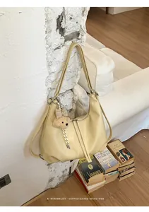 Zaino multifunzionale in pelle crema appeso a una parete bianca rustica con libri.
