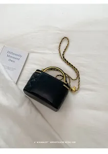 Close-up detail of a black quilted leather vanity bag with a gold chain strap on white fabric