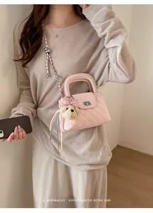 Close-up detail of a pink quilted handbag featuring a bear charm and elegant chain strap