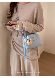 Detailed view of light blue quilted leather bag with cute plush bear charm and chain strap