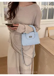 Stylish woman holding a light blue quilted chain handbag in a minimalist interior