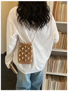 Bolso bandolera de paja hecho a mano con detalles de conchas mostrado en una modelo