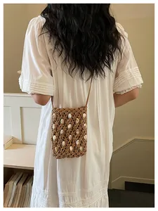 Bolso bandolera de paja tejido a mano con detalles de conchas blancas en modelo.