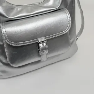 Detailed close-up of a silver metallic shoulder bag featuring a front pocket buckle