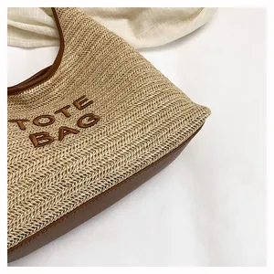 Close-up of a handwoven straw tote bag featuring detailed brown embroidery and leather trim.