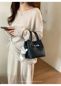 Close-up detail of a chic black bucket handbag with bear charm held by a model.