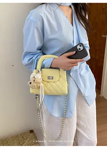 Model holding a yellow quilted handbag with chain strap and cute bear charm detail