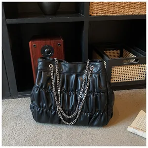 Large capacity black pleated tote bag with silver chain straps in a stylish home setting