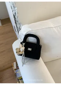 Close-up of black quilted handbag with teddy bear charm on a white sofa