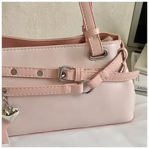 Close-up view of a pink underarm tote bag showing metal buckles and heart charm.