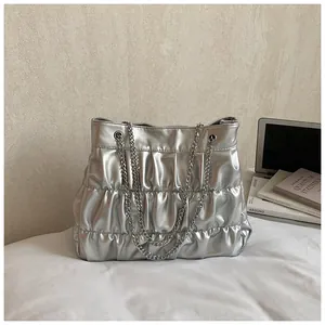 Detailed view of a silver metallic pleated tote bag with chain straps on a bed.