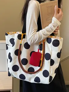 Grote canvas tote bag met zwarte stippen, kleurrijke geweven band en rood etui accessoire.