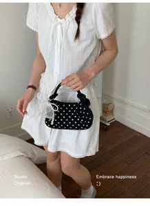 Small black polka dot dumpling handbag with white mesh bow and elegant pearl strap.