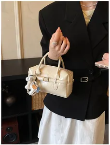 Detail of a minimalist cream glossy Boston bag with a cute dog charm held by a model.