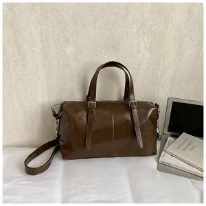 Sac polochon vintage marron foncé brillant avec bandoulière réglable sur scène de bureau