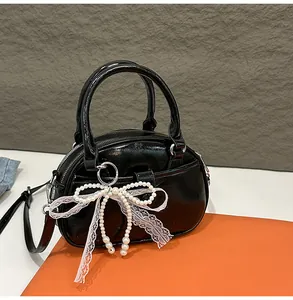 Detailed view of elegant black glossy handbag featuring a pearl bow and lace charm