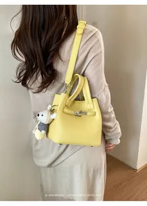 Stylish yellow textured leather bucket bag with cute bear charm shown on a model