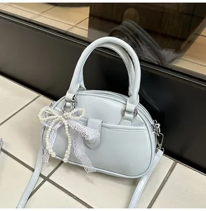 Close-up view of a chic light blue top handle bag featuring a delicate pearl bow and lace charm