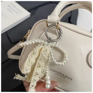 Close-up detail of cream handbag featuring elegant pearl bow and lace pendant