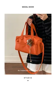 Model carrying a vibrant orange pebble-grain faux leather Boston bag with a cute charm.