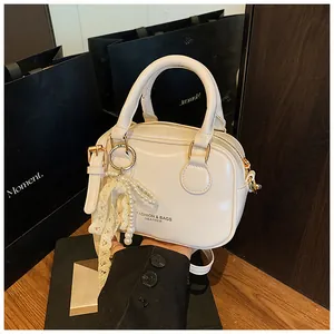 Close-up of a cream-colored leather handbag with elegant pearl and lace tassel charms.