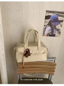 Cream-colored designer pillow tote bag with plush charm displayed on a modern chair.