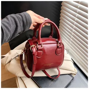 Close-up detail of a dark red glossy leather handbag held by hand over a beige blazer