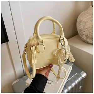 Detail view of a cream mini handbag featuring a decorative pearl and lace bow charm.