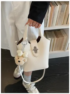 Detailed view of white lychee grain leather handbag featuring silver turn-lock and bear charm