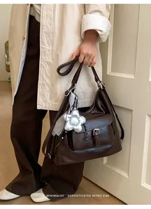 Detailed view of a dark brown leather tote bag featuring a stylish silver flower charm