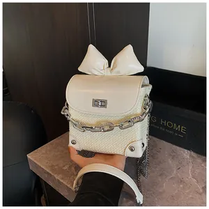 Close-up of a mini cream crossbody bag featuring a woven body and a large bow detail.